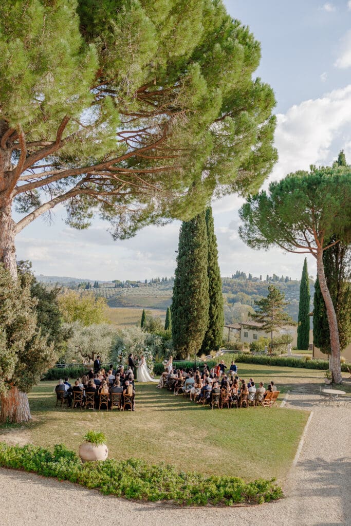 Elevated view of Hannah and Brandon's outdoor wedding ceremony at Tenuta di Sticciano framed by stone pines with the Valdelsa countryside stretching behind