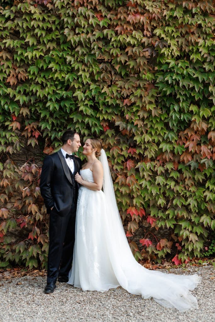 Hannah Chubb and Brandon Warner embracing in front of an autumn ivy wall turning red and green at Tenuta di Sticciano, Tuscany
