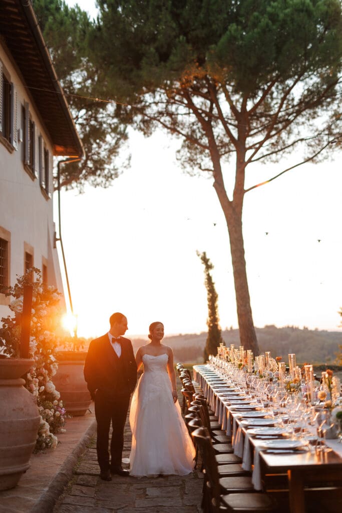 Hannah Chubb and Brandon Warner walking beside the long reception dinner table at blazing sunset at Tenuta di Sticciano, Tuscany