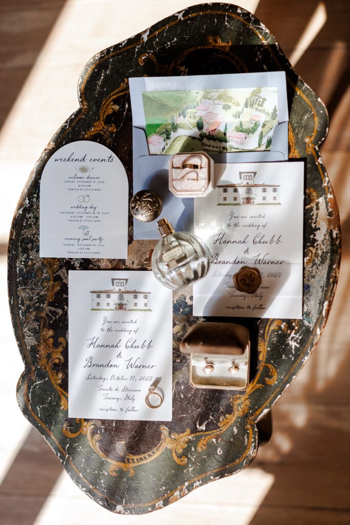 Wedding invitation suite for Hannah Chubb and Brandon Warner at Tenuta di Sticciano, Tuscany, October 2025, displayed on an antique Florentine table with rings and perfume
