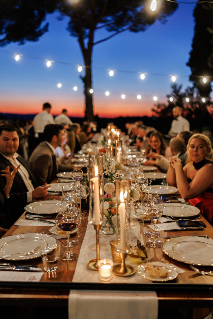 Wedding reception dinner at dusk with string lights and candles under the Tuscan sky