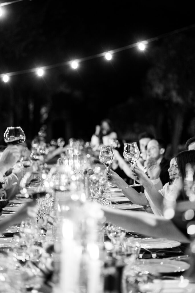 Guests raising wine glasses in a toast at the candlelit dinner, black and white