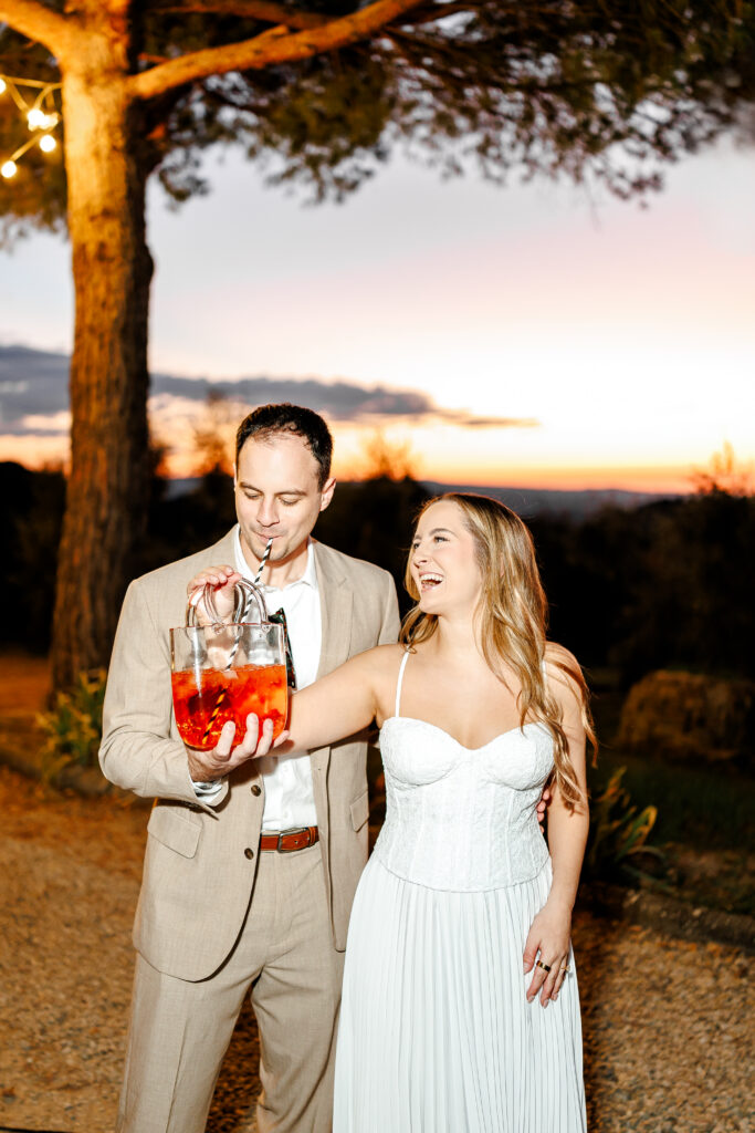 Hannah and Brandon laughing together at sunset with an Aperol spritz during their Tuscany wedding weekend welcome party