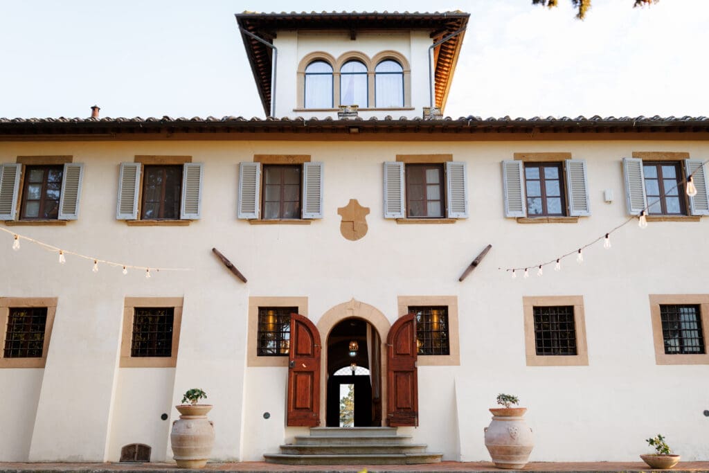 Tenuta di Sticciano villa exterior at golden hour with string lights and open arched doors for a destination wedding in Tuscany